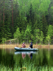 Fototapeta na wymiar Two men catch fish from an inflatable boat with fishing rods on the lake in the summer