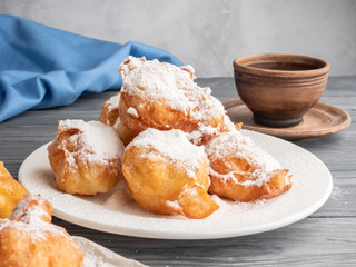 Beignet sprinkled with icing sugar on a wooden table with coffee and milk.