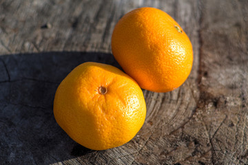 Ripe Mandarin fruit peeled open and place on old rustic look timber with group of mandarin fruits and leaves out of focus on the background