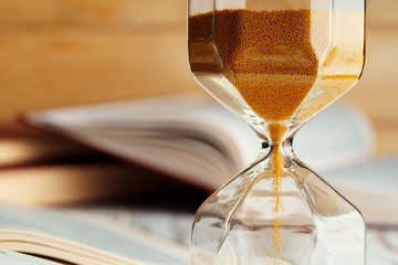 Sandglass on wooden table with opened book close up