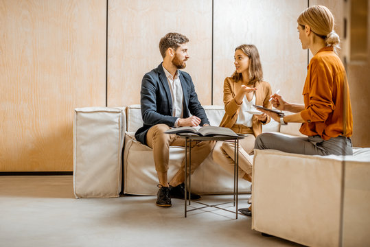 Young couple talking with a sales manager or real estate agent, sitting on the comfortable couch in the office