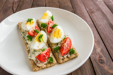 open crispbread sandwiches with boiled eggs fresh tomatoes cream cheese on white plate . healthy food