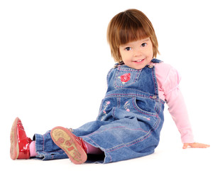 Small girl in jeans jumpsuit sitting on floor and smiling