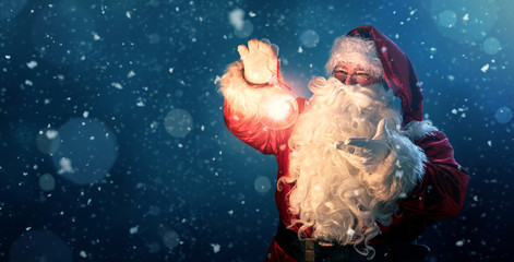 Happy Santa Claus holding glowing christmas ball over defocused blue background with copy space