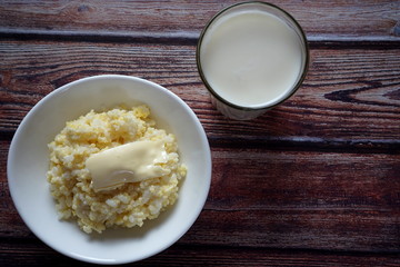 Porridge of rice and millet with butter and a glass of milk on a wooden table. Healthy diet