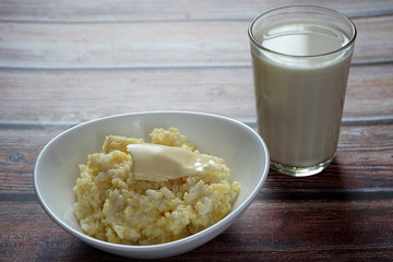 Porridge of rice and millet with butter and a glass of milk on a wooden table. Healthy diet