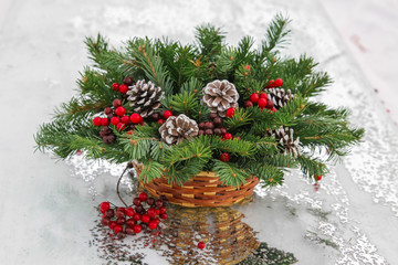 Closeup New Year wicker basket with snow covered spruce evergreen branches, cones and red berries.
