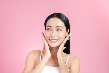 Beautiful Asian Girl touching her face and smiling, pampering her skin. Pink background