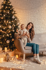 Obraz premium Happy family of mom with little baby hugging and celebrating new year in front of Christmas tree in decorated interior. Celebrating Christmas.