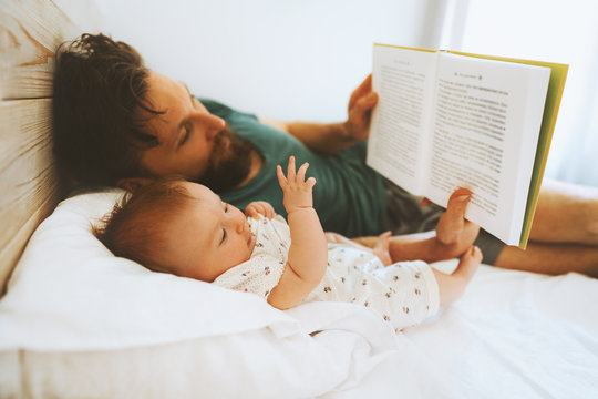 Family father and infant baby reading book fairytale laying on bed at home lifestyle dad and child daughter together parenthood childhood concept Fathers day holiday
