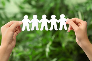 Woman holding paper people chain on blurred green background, closeup. Unity concept