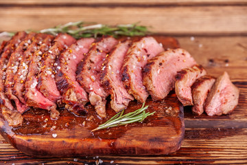 Chopped Grilled Steak Rib Eye on Rustic Cutting Board on Wooden Background. Juicy Medium Ribeye Steak with Spices and Rosemary. Concept of Delicious Meat Food