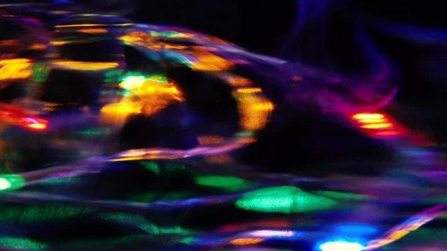 Colored Christmas lights shot through water tank with white paint drops and dark background on a Sony a7iii.