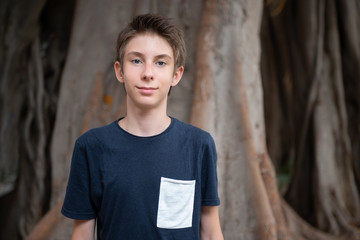 Handsome young boy at summer park. Beautiful calm smiling teen boy against nature background. Teenage lifestyle.