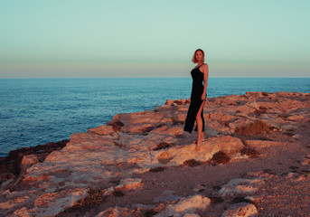 Woman wearing elegant summer black dress walking sea bank in Torrevieja, Spain. Ocean, coast, summer vacation, travel destination.