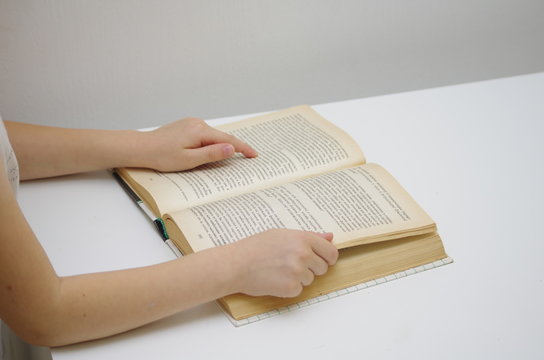 Little girl reads big book against white background and drives down lines with a finger