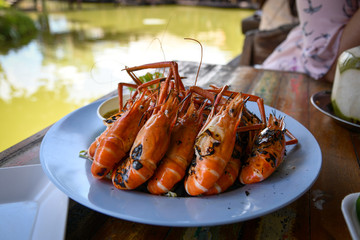 Grilled shrimps serve with thai spicy seafood sauce on blue plate on wooden table at riverside restaurant in Ayutthaya province, Thailand.