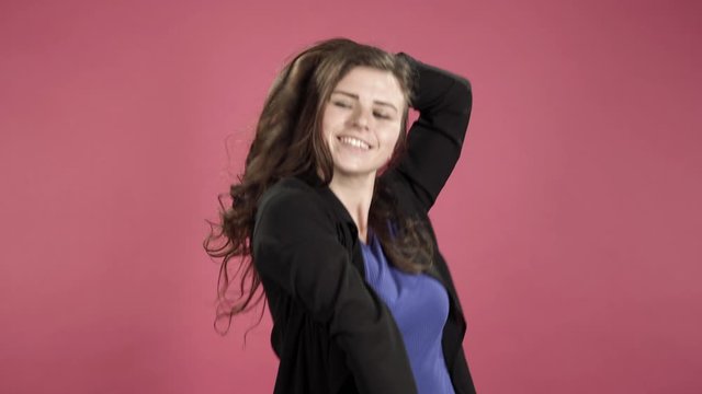 Young woman smiling and dancing in studio against pink background.