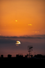 Sun appears from behind the clouds, above the city, roof top view. Summer sunrise or sunset. Orange sky color tones. Old town of Badalona, Spain