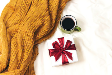Obraz na płótnie Canvas coffee cup and gift box above woolen scarf on bed, hello winter and christmas concept
