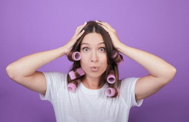 Fototapeta premium Funny girl with curlers clings to her head.