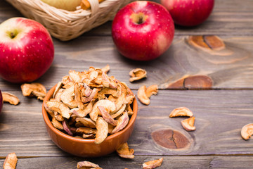 Sliced dried apples ready to eat in a bowl and fresh apples on a wooden table