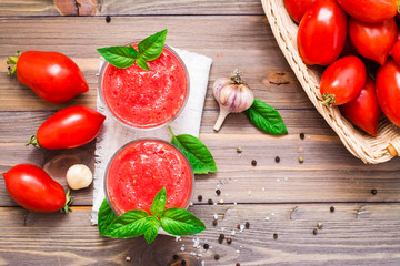 Blended fresh tomato juice with basil leaves in glasses and ingredients for its preparation on a wooden table. Top view