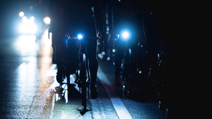 group of road bike riders at night, they turn on the headlights.noise in image. - Powered by Adobe