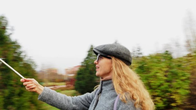 A young Caucasian girl-blogger walks in autumn Park, talking into the phone camera, leads the online broadcast, waving Hello to the audience. Technology and lifestyle concept through live streaming