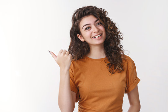 Girl inviting go together. Friendly charming smiling cute armenian woman tilting head pointing left thumb joyfully grinning asking you wanna visit cool place, recommending cafe, standing white wall