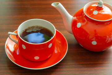 Cup of hot black tea and teapot with white polka dots on a wooden table. Tea time concept