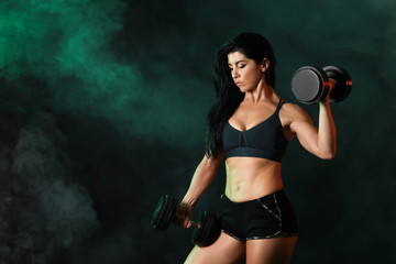 Fototapeta na wymiar Sporty muscular woman with dumbbells on dark background