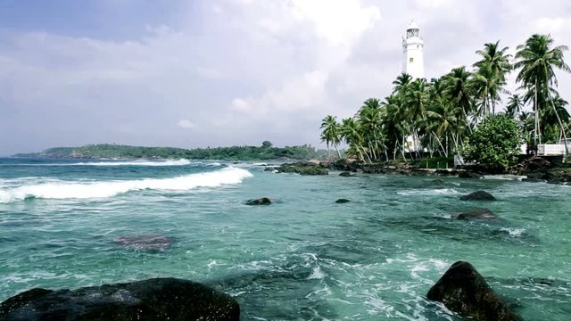 Beautiful bright colorful footage of lighthouse with palm trees in Dondra, Sri Lanka. Ocean waves rolling in, breaking.