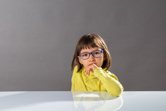 Cute Thinking Child With Eyeglasses Enjoying Thinking, Looking At Camera