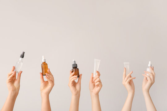 Female hands with different cosmetic products in bottles on grey background