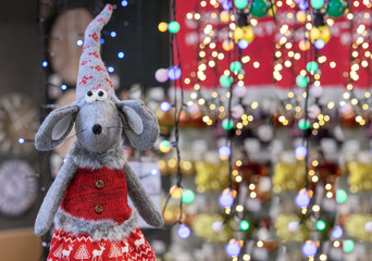 Toy mouse in knitted clothes on the background of festive garlands. Symbol of 2020.