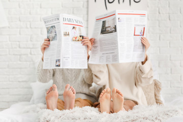 Beautiful young couple reading newspapers on bed at home