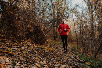 A guy in a red windbreaker runs in the autumn forest. © milogrodskiy