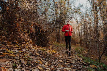 Fototapeta premium A guy in a red windbreaker runs in the autumn forest.
