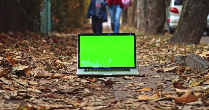 Green screen laptop computer outside with beautiful nature and children walking home from school on background. Chromakey display. Shopping. Business network application. Family app. Freelance working