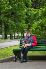 Obraz premium Happy smiling boy reading a book on bench in park