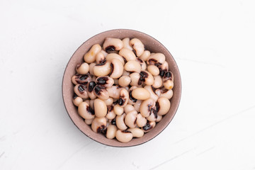Cooked Fradinho beans in a black clay pot, isolated on a white background.
