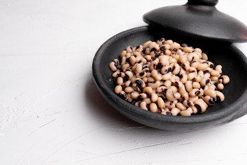 Cooked Fradinho beans in a black clay pot, isolated on a white background.