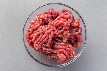 Fresh ground beef lies in a large glass bowl on a gray background