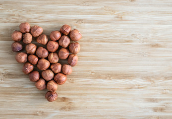 Hazelnuts laid out in the shape of a heart on a light brown background, top view