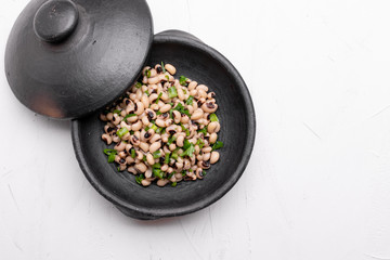 Cooked Fradinho beans in a black clay pot, isolated on a white background.