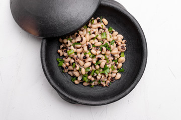 Cooked Fradinho beans in a black clay pot, isolated on a white background.