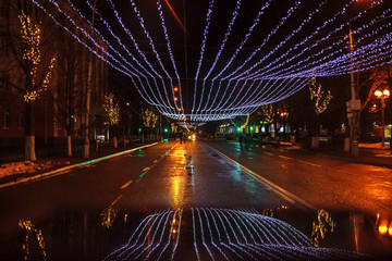 Night city landscape on Christmas and new year with lights and garlands on almost empty Avenue after rain with reflections