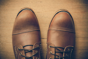 ฺBrown leather shoes with vintage camera on a wooden floor.Brown vintage leather boots aligned selective focus.Men leather shoes 