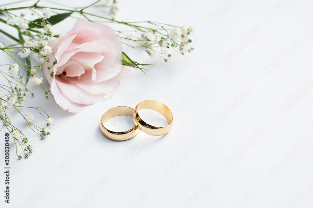 Wall mural Pink flowers and two golden wedding rings on white background.